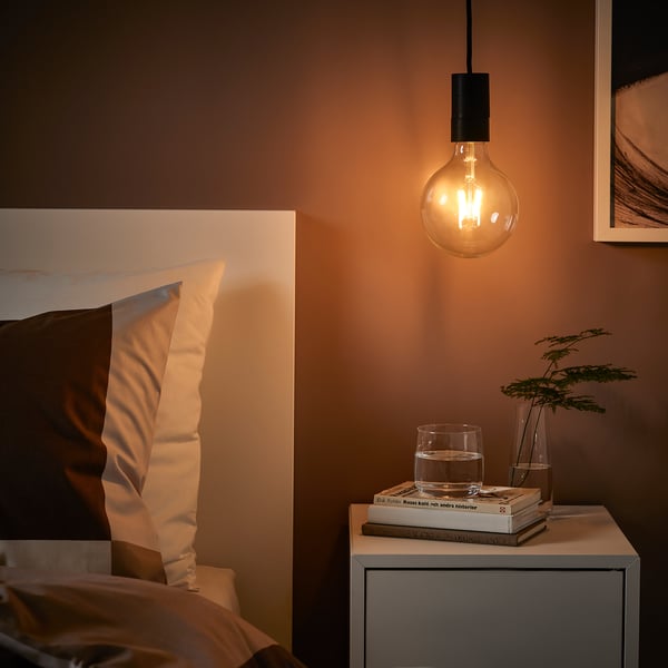 Cozy bedroom with SUNNEBY lamp, nightstand, books, glass, plant.