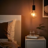 Cozy bedroom with SUNNEBY lamp, nightstand, books, glass, plant.