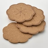 Four round cork coasters with scalloped edges stacked neatly, showing natural texture and durable quality.
