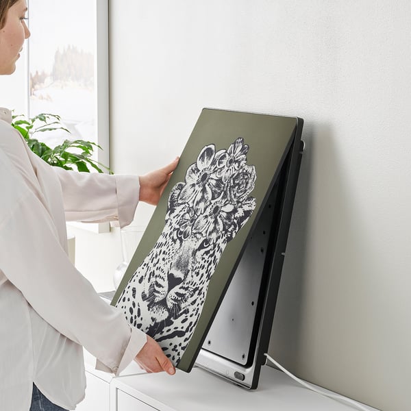 Person holding a SYMFONISK picture frame speaker with interchangeable art panel.