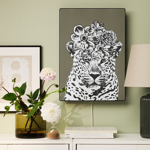 Black & white leopard print frame with flowers on shelf next to vase, lamp, and books.