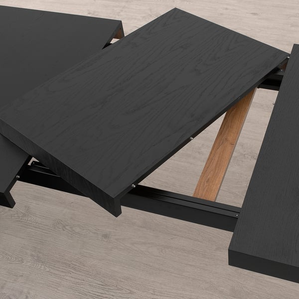 Black extendable dining table with metal frame, shown with extension leaf stored underneath. Adjusts to seat 4-6 people.