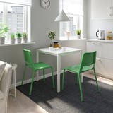 Compact dining nook with white table, two green stackable chairs, city view.
