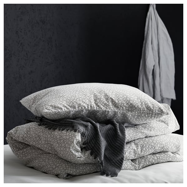 A stack of black and white patterned pillows, one with a draped gray blanket, against a dark wall.
