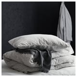 A stack of black and white patterned pillows, one with a draped gray blanket, against a dark wall.