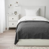 Bed with TJÄRBLOMSTER grey fleece blanket; single size near white nightstand with lamp.