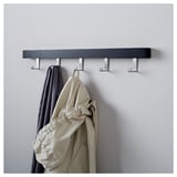 A wall-mounted coat rack, TJUSIG series, holds a gray jacket and beige coat on its metal hooks. The dark wooden shelf organizes clothing efficiently.