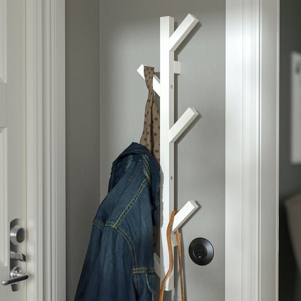 White wooden coat rack on wall holds jacket and hat.