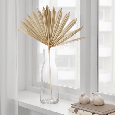 Glass vase with dried palm leaf on windowsill.