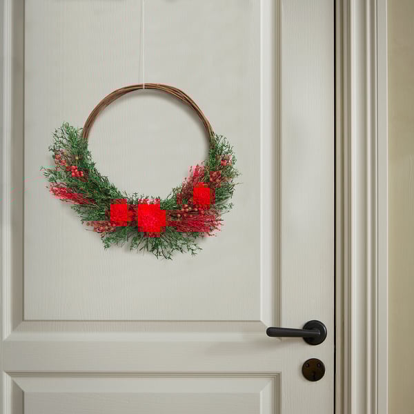 Wreath on door. Red flowers, green leaves, circular frame. Decorative, natural, inviting.
