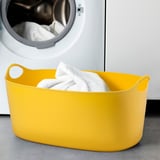 Bright yellow TORKIS laundry basket near open dryer with white towels.