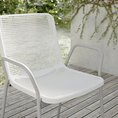 Two white TORPARÖ chairs sit on a wooden deck, featuring a perforated seat and back design, ideal for outdoor use.