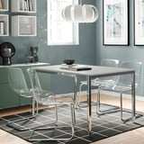 Modern dining set with clear chairs around white TORSBY table, chrome legs, gray rug, minimalist art.