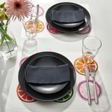 Brightly colored place mats with citrus slices create cheerful table settings. Black plates, cutlery, and glasses complete the modern look.