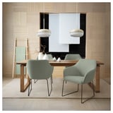 Modern dining room with TOSSBERG green chairs, wooden table, and pendant lights against a textured wall.