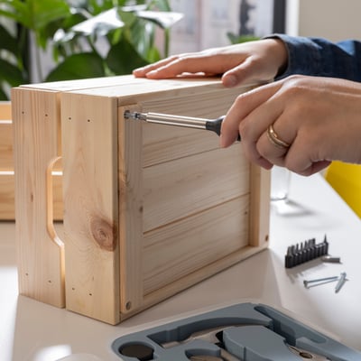 Person using screwdriver from TRIXIG toolbox to assemble wooden box.