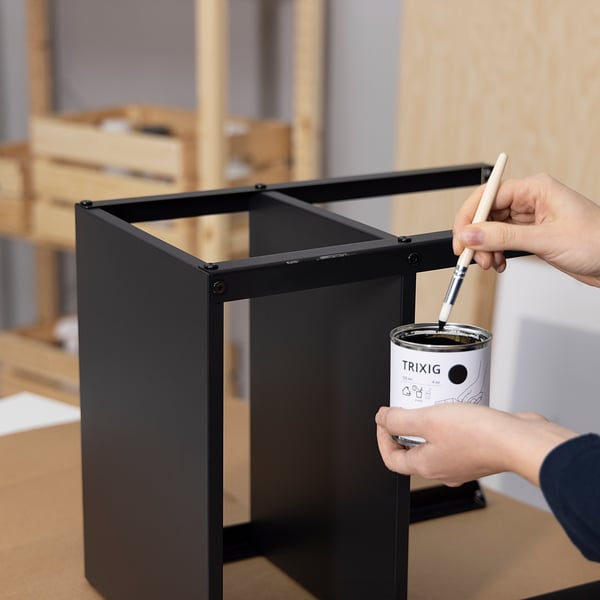 Person dips brush into TRIXIG paint, applying it to black furniture frame.