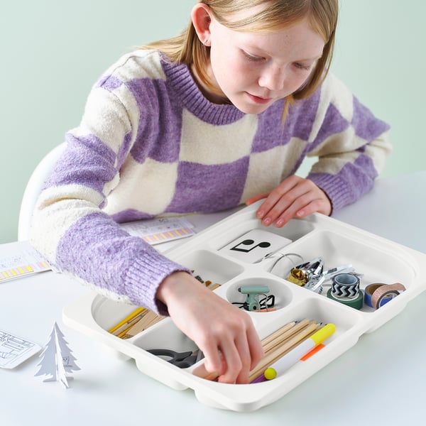A girl organizes school supplies in a TROFAST tray with compartments.