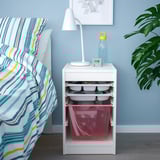 Bedside TROFAST unit with lamp, bottle, clock; colorful bedspread, plant.