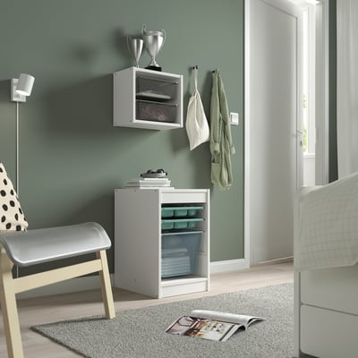 Room with TROFAST storage unit. White, light blue baskets, between chair and door. Green walls, light floor.