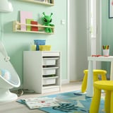 Kids room with TROFAST storage, colorful boxes, yellow chair, table, toys.