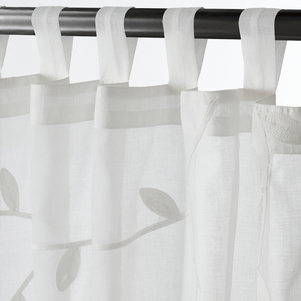 White sheer curtains with leaf patterns hang from tabs on a black rod.