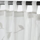 White sheer curtains with leaf patterns hang from tabs on a black rod.
