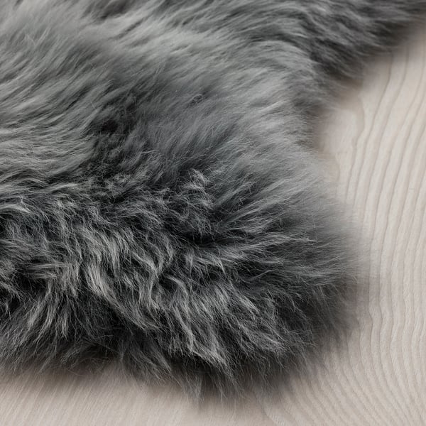 Fluffy, dark gray sheepskin rug on light wooden floor. Soft texture, inviting for touch.