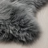 Fluffy, dark gray sheepskin rug on light wooden floor. Soft texture, inviting for touch.