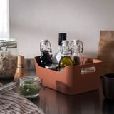 Orange recycled plastic box with handles holding glass bottles on kitchen counter.