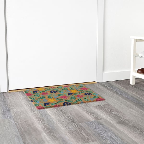 Brightly colored floral doormat at a white door entrance on gray wood floor.