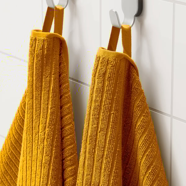 Two bright yellow VÅGSJÖN towels hang neatly on hooks. Soft, absorbent cotton dries quickly, adding vibrant colour to the bathroom.