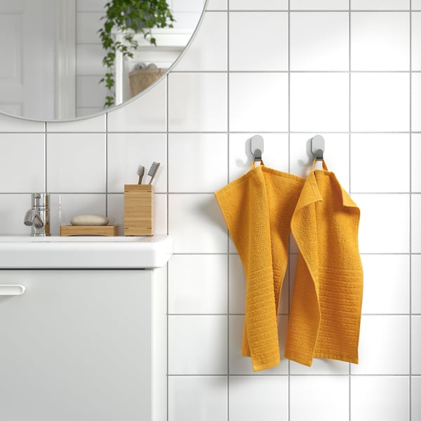 Yellow VÅGSJÖN towel on hooks beside white-tiled wall in minimalist bathroom.