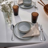 Table set with gray dishes, silverware, striped napkins, brown cups, and a vase of babys breath.