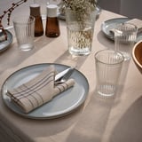 Table setting with blue plates, striped napkins, fluted glasses, cream plates, bottles, and white flowers.