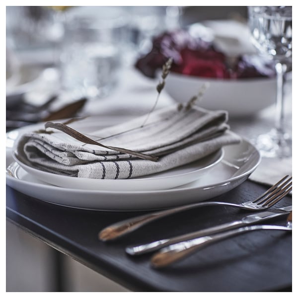 Dining table with folded VÅRARV cotton napkins on plates and cutlery.