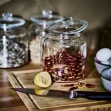 Wooden cutting board with knife, lemon half, and jar of dried chilies; glass jars in background.