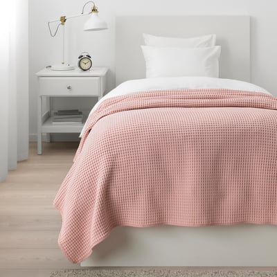 Cozy bedroom with light pink bedspread, gray headboard, nightstand, and lamp.