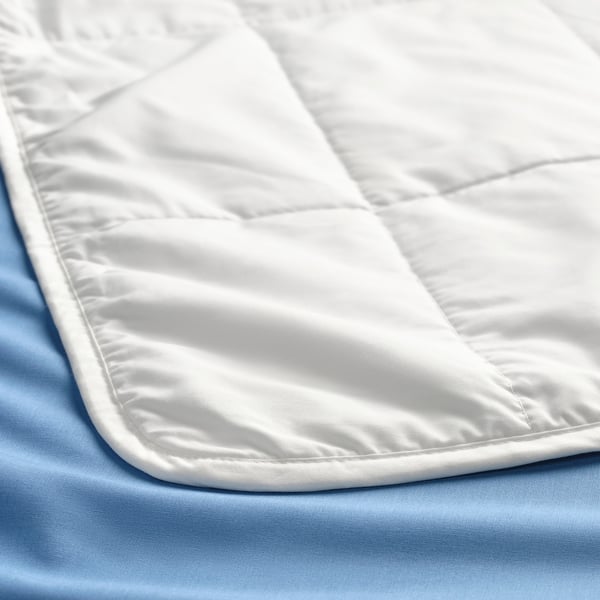 Close-up of a white comforter on blue sheet, showcasing texture and stitching detail.