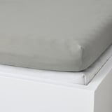 Grey fitted sheet on white bed, showcasing its elastic corner for secure fit.