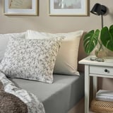 Cosy bedroom setup: grey VÅRVIAL cotton sheets on bed, white pillows, small bedside table with lamp, plant, and books.