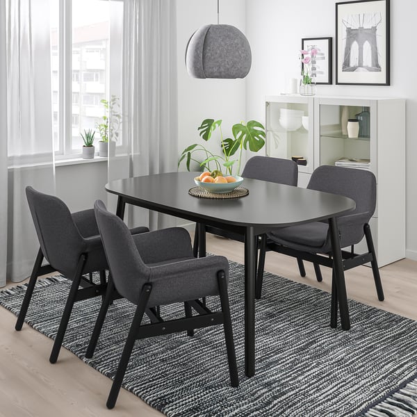 Modern dining setup with black VEDBO table, four grey chairs, under hanging lamp, near large window.