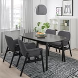 Modern dining setup with black VEDBO table, four grey chairs, under hanging lamp, near large window.