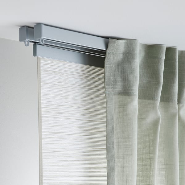 Gray curtain rail mounted on white wall, supporting light green curtains. Easy to assemble and flexible for tricky spaces.