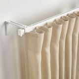 Curtain rod holds light or heavy drapes. Wall-mounted, lets light in or blocks it. Via white rail and hooks.