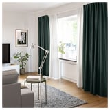 Modern living room with VIDGA curtains in green and white, wooden floor, grey couch, and plants.