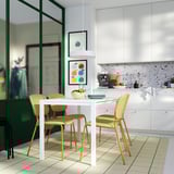 Modern kitchen with white table, four yellow chairs, foam-padded seats, and green-framed glass wall.
