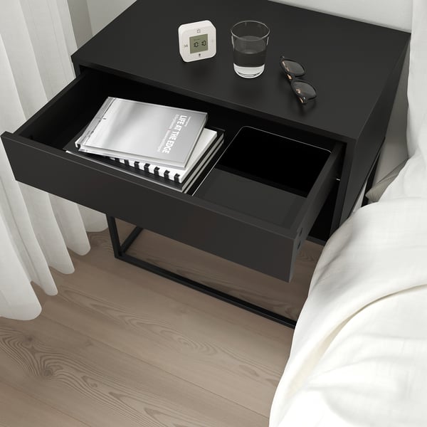 Black bedside table with open drawer showing books. Soft-closing feature highlighted.
