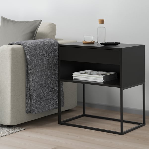 Black side table with 2 shelves, next to sofa, holds magazines, minimalist.