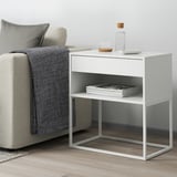 White VIKHAMMER side table with drawer and shelf next to gray chair, sleek design.